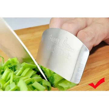 Protector de dedos de acero inoxidable protegiendo mano al cortar verduras en cocina
